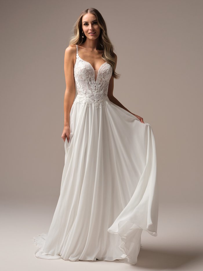 Bride wearing the Finley A-line wedding dress by Rebecca Ingram, featuring a beaded floral lace bodice with a plunging neckline and a flowing chiffon skirt.