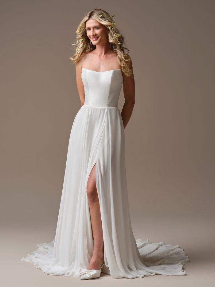 Georgina by Rebecca Ingram A-line wedding dress featuring a strapless square neckline, flowing chiffon skirt, thigh-high slit, minimalist bodice, and romantic sweep train.