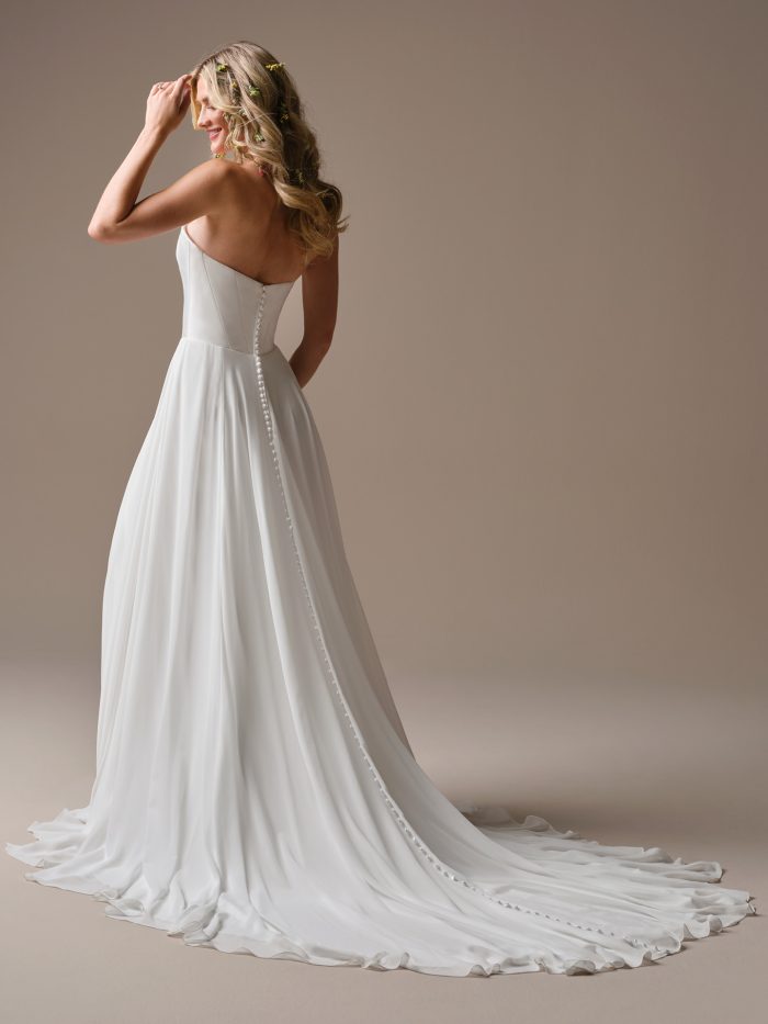 Georgina by Rebecca Ingram chiffon A-line wedding dress with a strapless square neckline, covered button back detail, flowing skirt, thigh-high slit, and extended train.