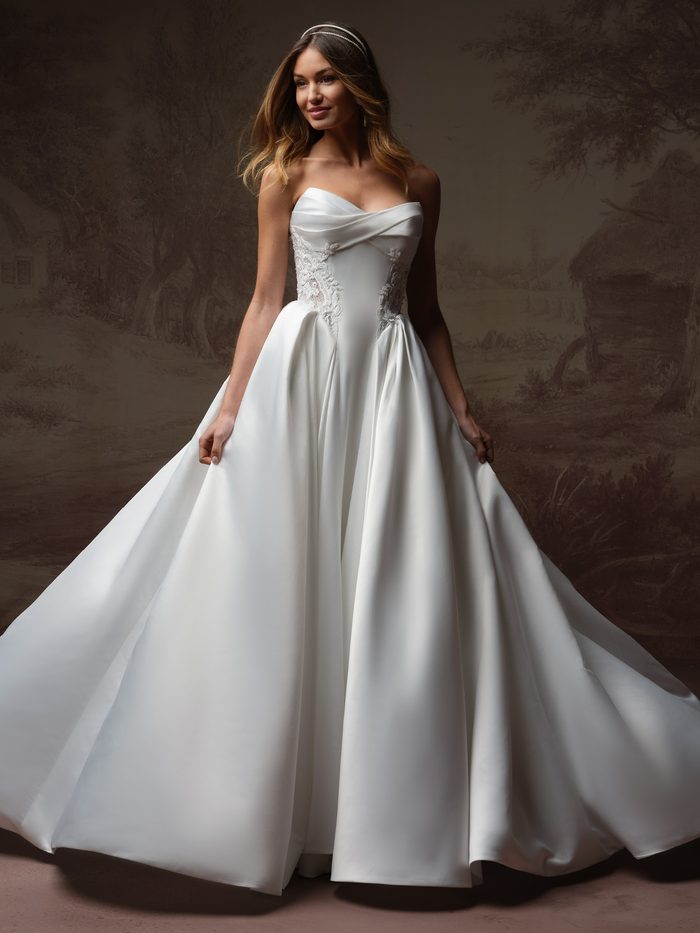Bride wearing the Gigi ballgown wedding dress by Rebecca Ingram, featuring a strapless draped satin bodice with lace side accents and a full satin ballgown skirt.