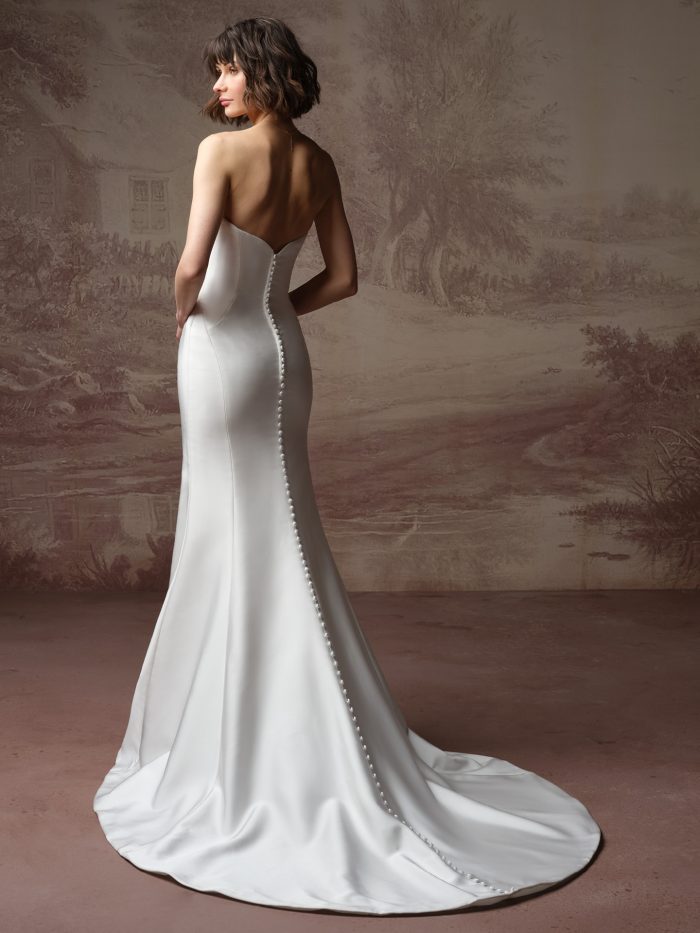 Kayla by Rebecca Ingram satin wedding gown with a low back, covered buttons, figure-flattering fit-and-flare silhouette, and flowing train.