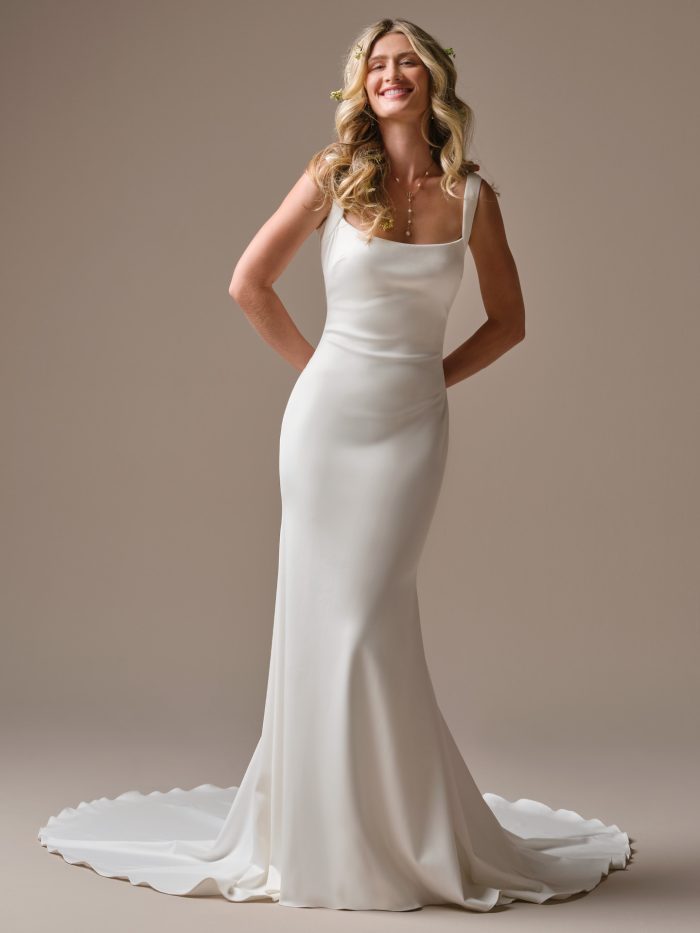 Lucille by Rebecca Ingram sheath wedding dress featuring a square neckline, minimalist crepe fabric, wide shoulder straps, fitted silhouette, and sweep train.