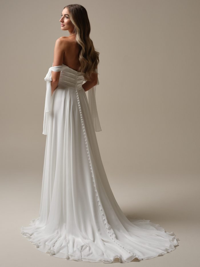 Melody by Rebecca Ingram chiffon A-line wedding dress with detachable off-the-shoulder sleeves, covered button back detail, flowing skirt, thigh-high slit, and extended train.