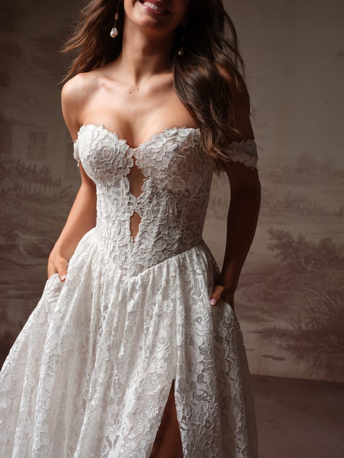 Close-up of a bride wearing the Narelle wedding dress by Rebecca Ingram, showing the lace off-the-shoulder bodice with keyhole detailing and floral lace skirt.