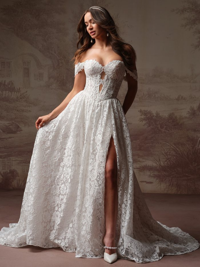 Bride wearing Narelle by Rebecca Ingram, a boho lace A-line wedding dress with off-the-shoulder cap sleeves, lace-up bodice detail, and a front leg slit.