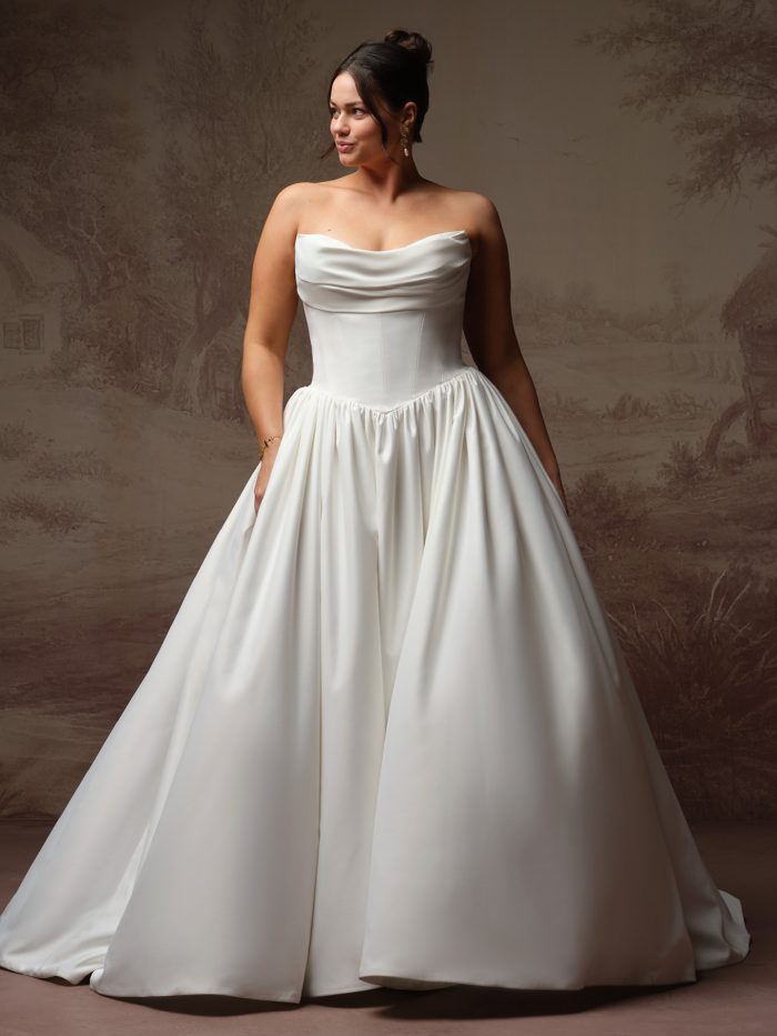 Vanessa by Rebecca Ingram Curve ballgown wedding dress featuring a draped strapless neckline, structured satin bodice, gathered waistline, hidden pockets, and a full satin skirt.