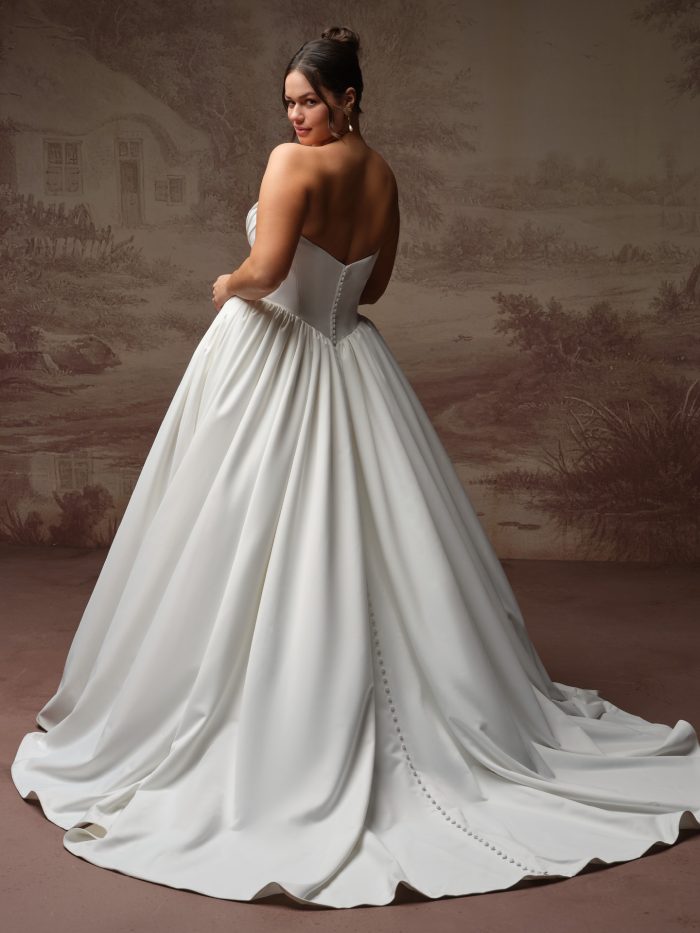 Vanessa by Rebecca Ingram Curve satin ballgown wedding dress with a low strapless back, covered button detailing, voluminous gathered skirt, and extended train.