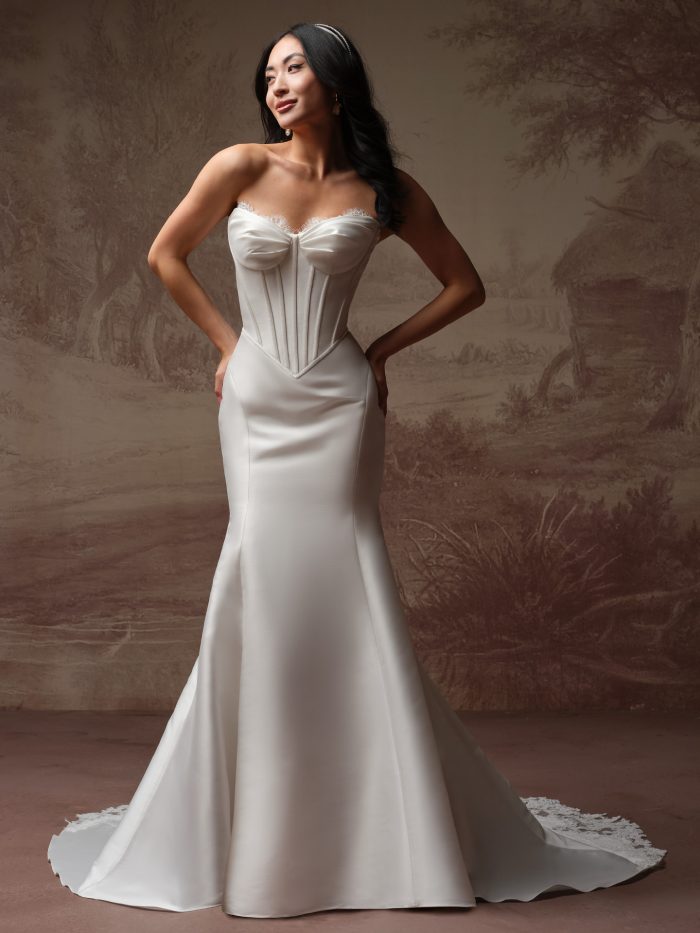 Front view of a bride wearing the Zorina Lane fit-and-flare wedding dress by Rebecca Ingram, featuring a strapless satin corset bodice with lace-trimmed neckline and a flared skirt with a lace-edged train.
