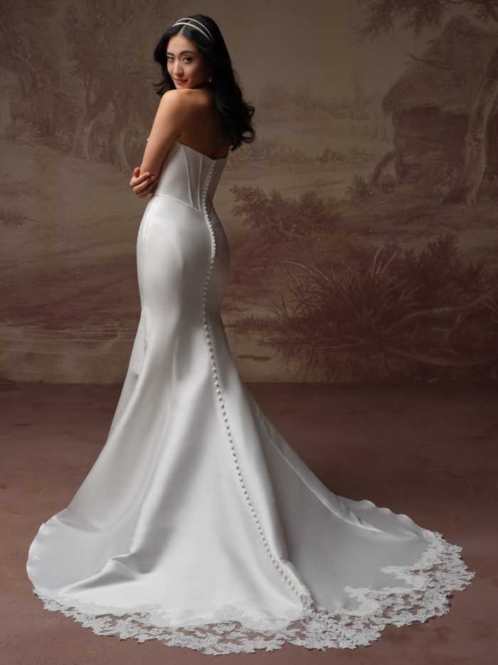 Back view of the Zorina Lane fit-and-flare wedding dress by Rebecca Ingram, showing the fitted corset back with covered buttons and a flowing train edged in lace.