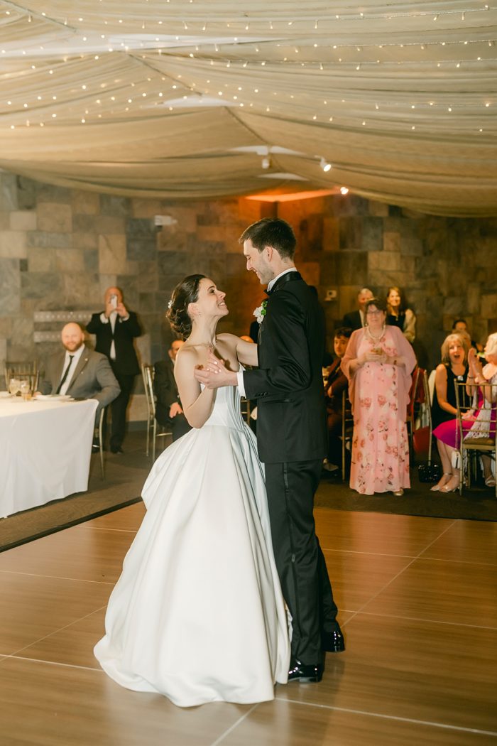 Wedding photo of a bride and groom sharing their first dance at their reception, the bride wearing a strapless satin ballgown wedding dress by Maggie Sottero.
