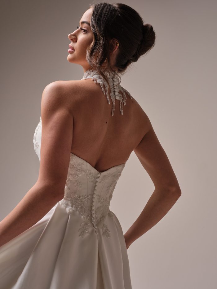 Amadora A-line wedding dress by Sottero and Midgley shown from the back, highlighting a strapless satin bodice with shimmering lace appliqués, covered buttons, and an embellished floral choker with delicate beaded drops.
