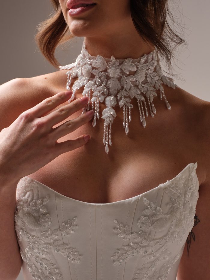 Close-up of the Amadora choker by Sottero and Midgley, a statement lace choker with beaded floral appliqués and cascading pearl fringe, paired with a matching beaded and lace strapless wedding dress.