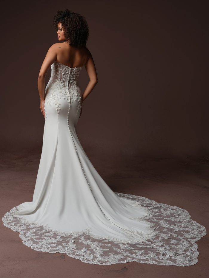 Back view of bride wearing the Blair strapless sheath wedding dress by Sottero and Midgley, featuring an illusion lace corset back, covered button closure, and an illusion lace train.