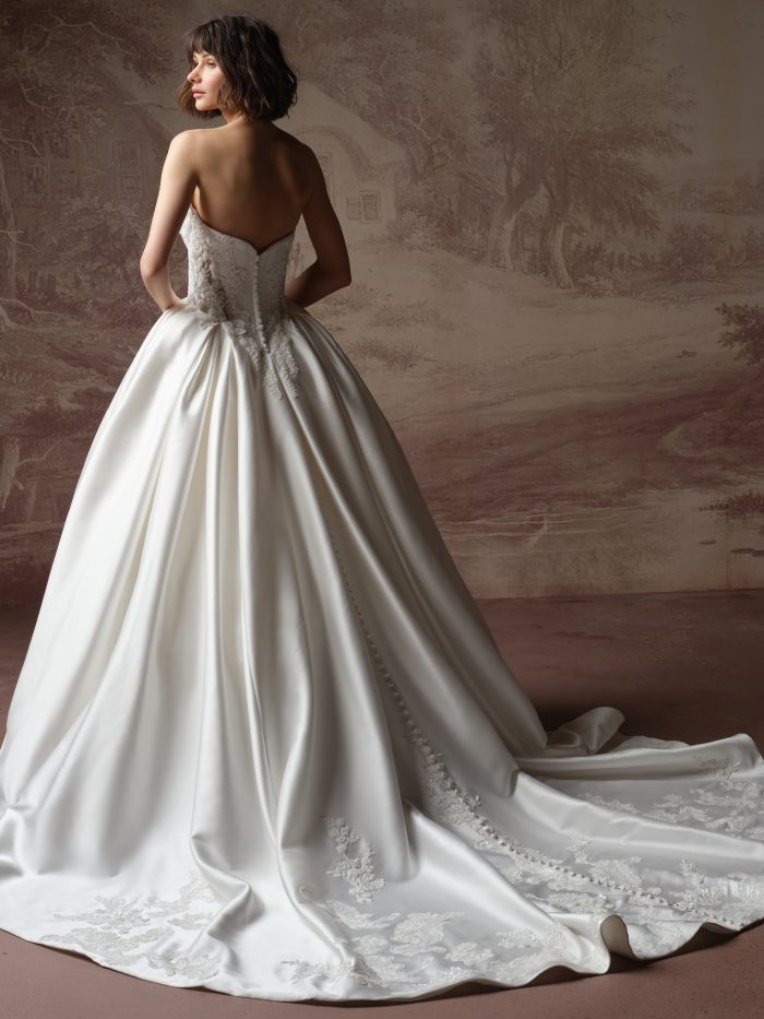 Back view of bride wearing the Burke Lane strapless satin ballgown wedding dress by Sottero and Midgley, featuring a lace bodice, sweetheart back neckline, covered button closure, and an embellished train.
