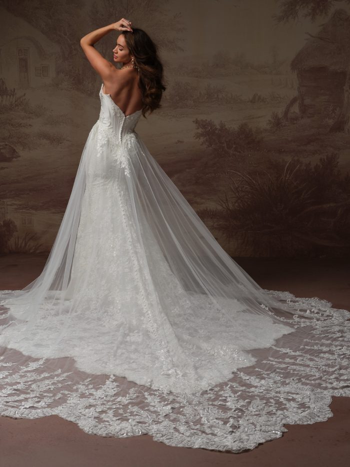 Back view of bride wearing the Eirawen fit-and-flare wedding dress with detachable tulle overskirt bridal train by Sottero and Midgley, showing the sheer train layered over the lace gown with a scalloped lace hem.