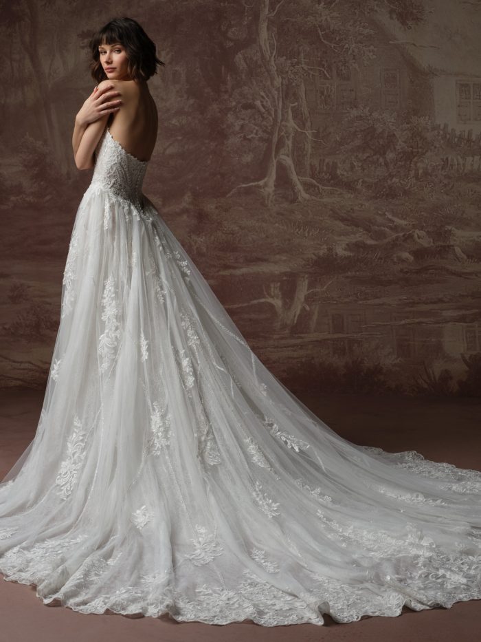 Back view of the Hester wedding dress by Sottero and Midgley, showing the open corset back, button detail, and detachable overskirt with lace train.