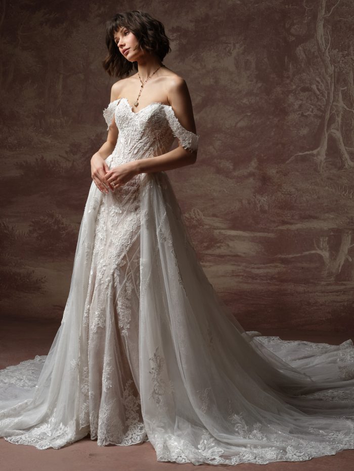 Bride wearing Hester by Sottero and Midgley, a lace wedding dress with off-the-shoulder cap sleeves and a detachable overskirt train.