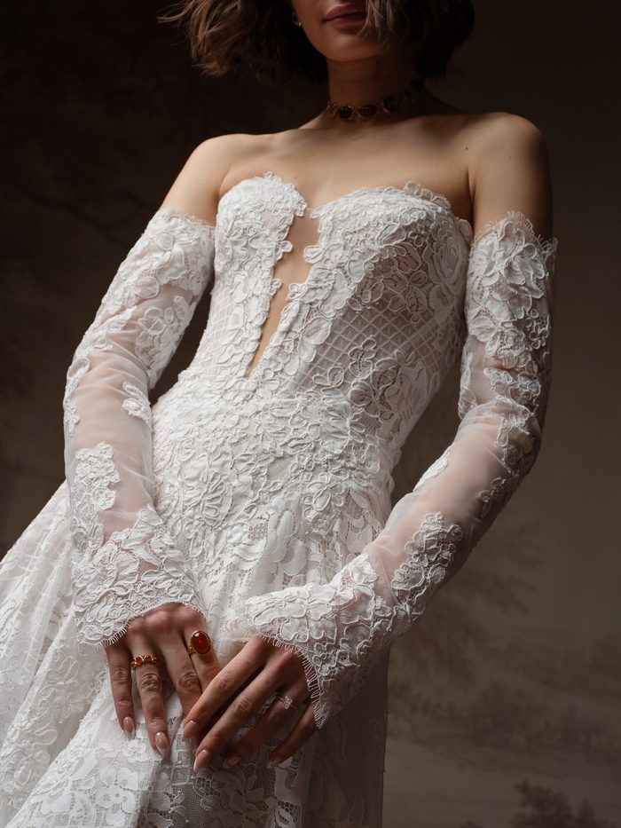 Close-up of the Keeva A-line wedding dress by Sottero and Midgley, showing the plunging lace bodice with detachable long lace gloves.