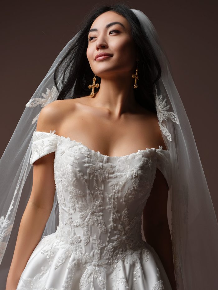 Close-up of the Lucinde wedding dress by Sottero and Midgley, showing the beaded floral lace bodice and off-the-shoulder cap sleeve draping.