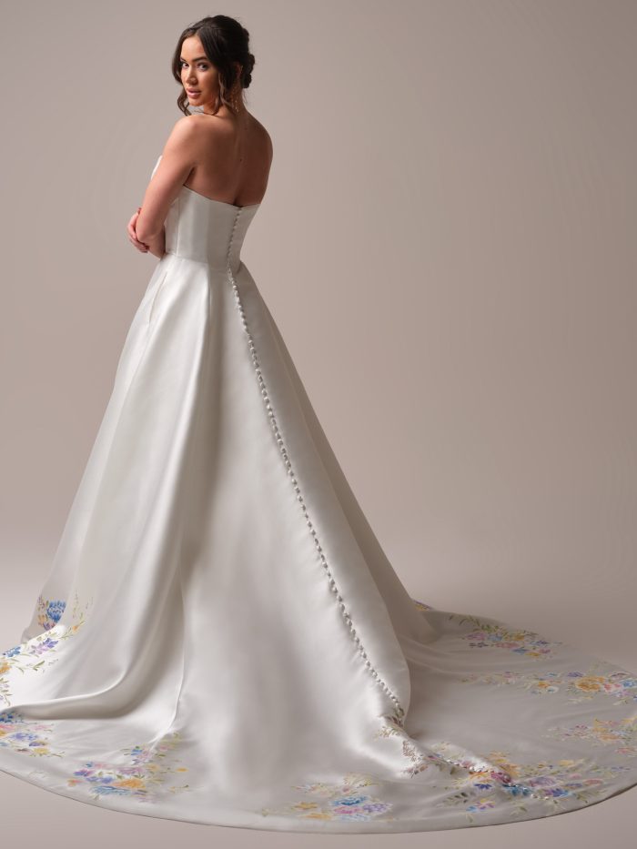 Back view of the Radiance A-line wedding dress by Sottero and Midgley, showing the strapless satin bodice with a row of covered buttons and a flowing train accented with the same watercolor floral print.