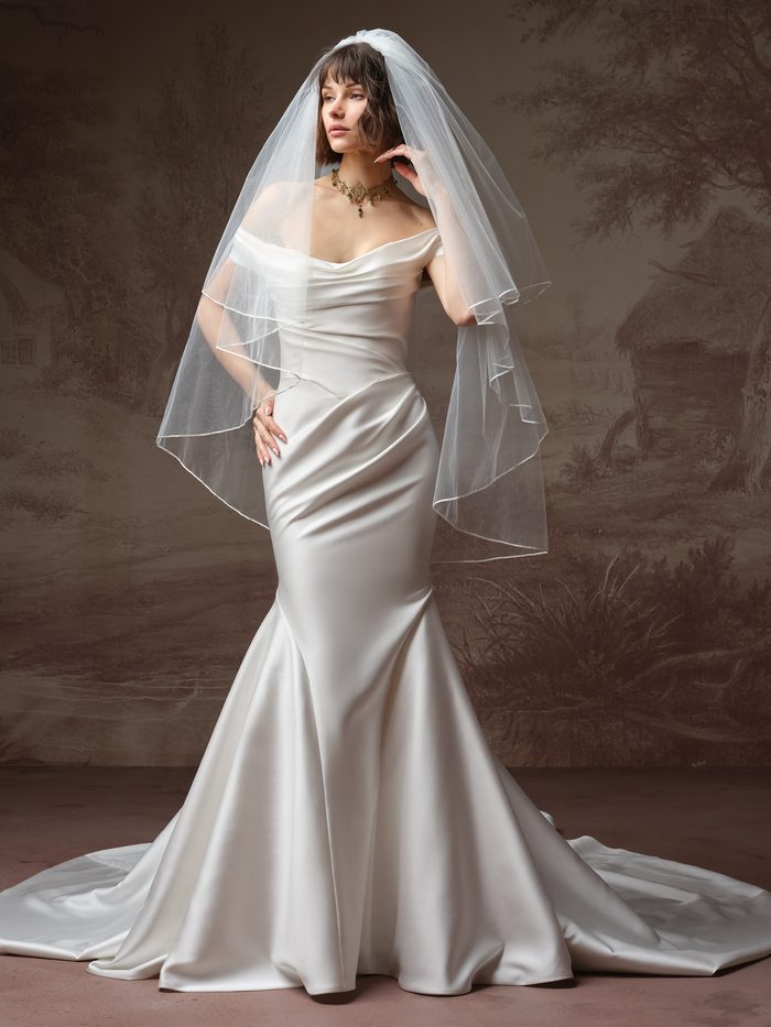 Bride wearing the Recine fit-and-flare wedding dress by Sottero and Midgley, featuring an off-the-shoulder draped satin bodice, a ruched waist, and a fitted satin mermaid skirt with a train, styled with a tiered veil.
