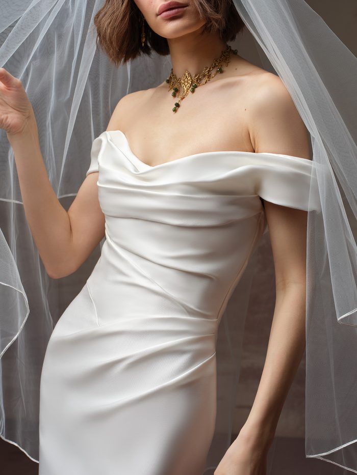 Close-up of the Recine fit-and-flare wedding dress by Sottero and Midgley, showing the off-the-shoulder draped satin bodice with ruched detailing at the waist.