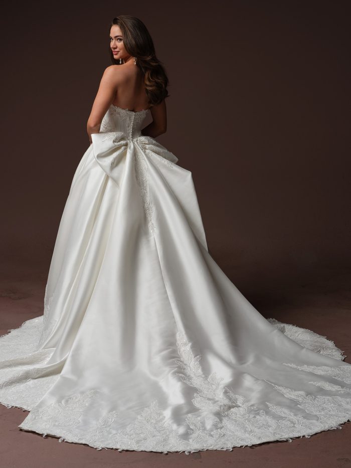 Back view of the Sandrine ballgown wedding dress by Sottero and Midgley, showing the fitted lace-appliquéd bodice, a large bow accent at the waist, and a dramatic satin train trimmed in lace.