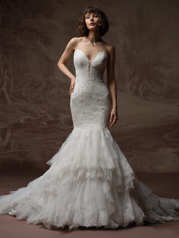 Bride wearing the Sauvignon fit-and-flare wedding dress by Sottero and Midgley, featuring a strapless lace bodice with a plunging sweetheart neckline and a tiered tulle mermaid skirt with a train.