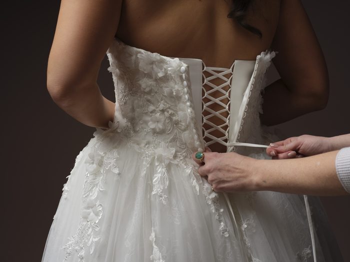 Close-up back view of the Benton wedding dress, featuring a lace-up corset closure, dimensional floral lace appliqués, and a voluminous tulle skirt. Hands adjust the corset lacing to showcase the gown's customizable fit and detailed bridal craftsmanship.