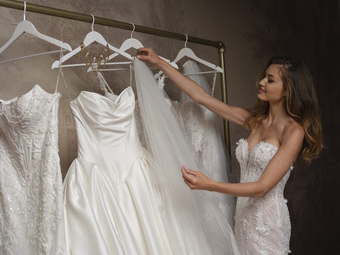 Person reviewing bridal gowns and a veil on a garment rack, comparing styles for a wedding reception look.
