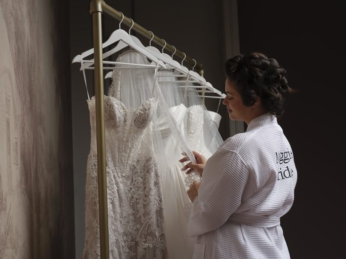 Bride-to-be reviewing wedding dresses and accessories on a garment rack while selecting a reception dress.