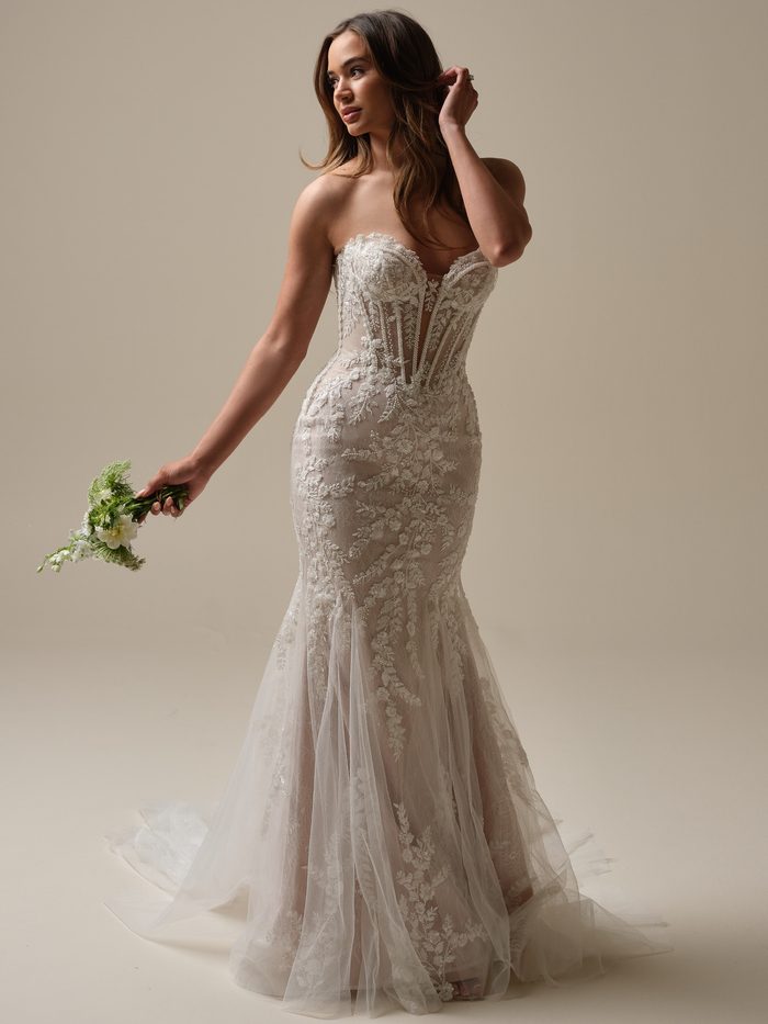 Full-length view of the Maggie Sottero Benjie fit-and-flare wedding dress in blush and ivory, showcasing a strapless sweetheart neckline, sheer corset-inspired bodice with intricate lace embroidery, fitted silhouette, and a flowing tulle skirt accented with floral lace appliqués.