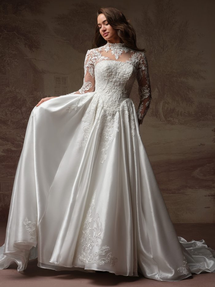 Dahlia by Maggie Sottero ballgown wedding dress featuring a high illusion neckline, long sheer lace sleeves, and intricate embroidered appliqués cascading across the fitted bodice and full satin skirt. Front view highlights the dramatic silhouette and ornate detailing in a studio setting.