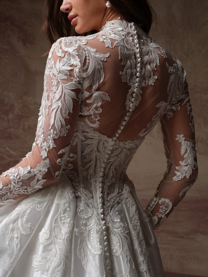 Back view of the Maggie Sottero Dahlia ballgown wedding dress in ivory, showcasing illusion lace long sleeves, a sheer lace back with button closure, a fitted corset bodice, and a full satin skirt adorned with delicate embroidered lace motifs.