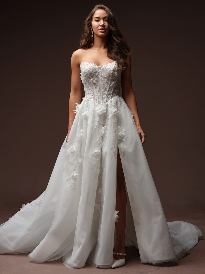 Fern by Maggie Sottero A-line wedding dress with floral lace appliqués, a strapless corset bodice, and a front slit.