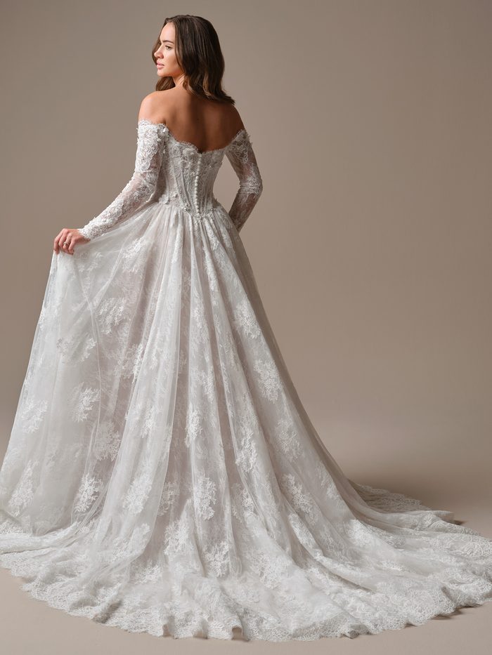 Back view of the Kitaro by Maggie Sottero ballgown wedding dress, showcasing an off-the-shoulder lace bodice, covered button detailing, long sheer lace sleeves, and a full lace skirt that extends into a dramatic cathedral-length train. Studio portrait emphasizing the gown’s volume and lace texture.
