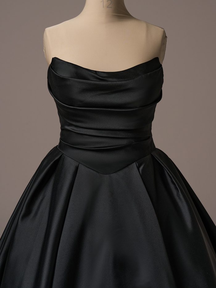 Close-up front view of the Maggie Sottero Maureen ballgown wedding dress in black, featuring a strapless draped neckline, softly ruched satin bodice, dropped waist detail, and a voluminous satin skirt with structured pleats.