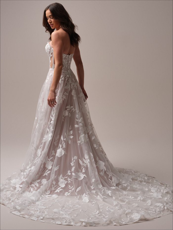Back view of the Natalie by Maggie Sottero A-line wedding dress with floral lace appliqués, a sheer bodice, and a flowing skirt that extends into a sweeping lace-trimmed train. Studio portrait highlighting the gown's silhouette and train details.