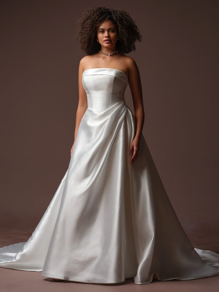 Agatha by Rebecca Ingram A-line wedding dress with a strapless neckline, draped satin skirt, and pockets.