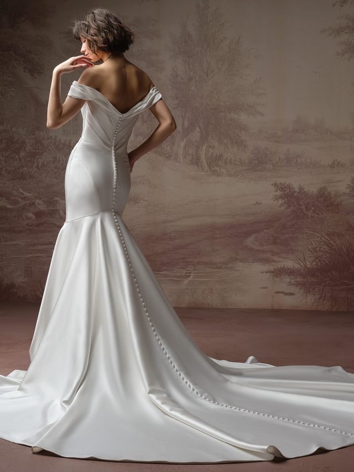 Back view of the Recine wedding dress featuring an off-the-shoulder neckline, button detail, and extended train.