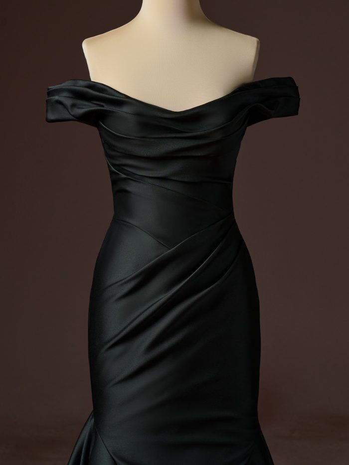 Close-up front view of the Sottero and Midgley Recine fit-and-flare wedding dress in black, featuring an off-the-shoulder draped satin neckline, softly ruched bodice, asymmetrical wrapped waist detailing, and a sleek fitted silhouette that flares below the hips.
