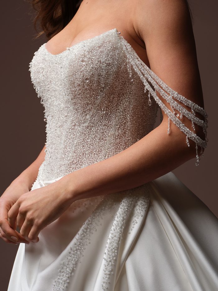 Close-up of the Rumi wedding dress featuring a beaded strapless bodice and crystal-draped sleeve detail.