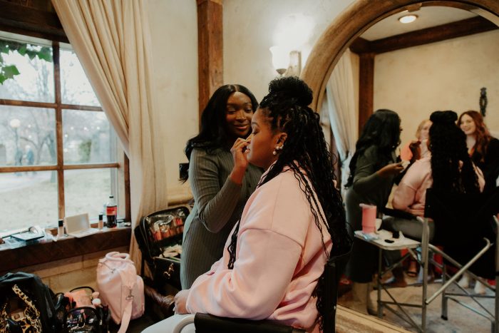 Bride getting her makeup touched up by a makeup artist while getting ready with her bridal party on her wedding day.