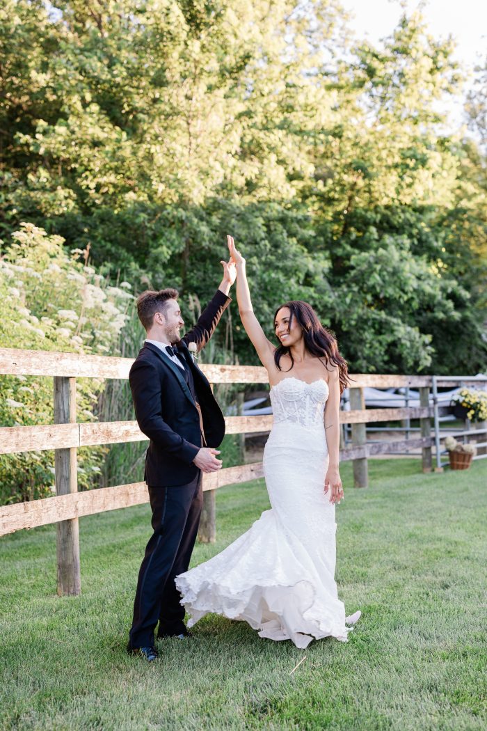 Bride in a strapless stretch fabric wedding dress with a lace corset bodice and fitted silhouette dances with the groom at an outdoor wedding.