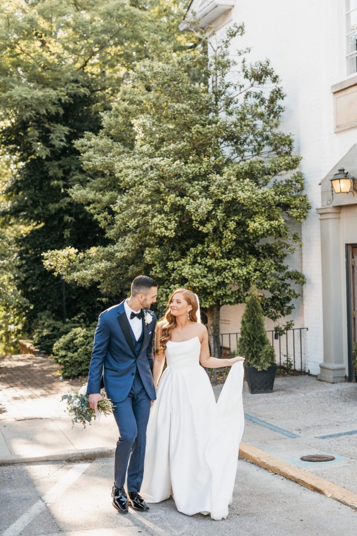 Bride and groom walk together outdoors, with the bride wearing a strapless Mikado wedding dress featuring a structured bodice and full A-line skirt.